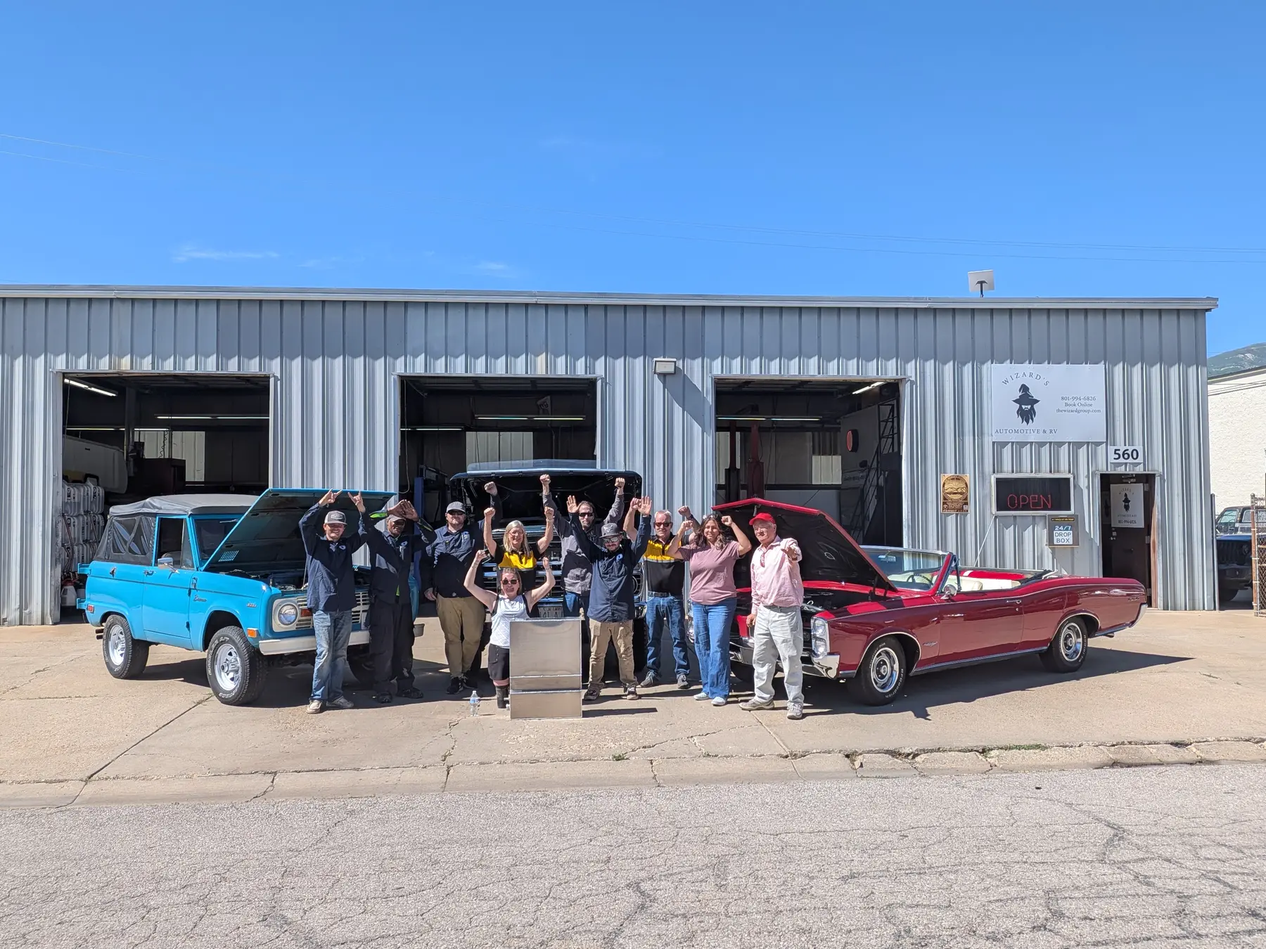 Wizard's Automotive and RV team standing outside the Bountiful shop between a blue classic truck and a red classic car